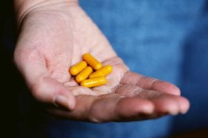 A person’s hand holding turmeric supplement capsules in their hand